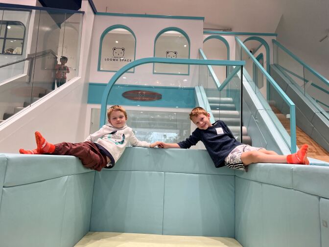 Two males with light skin tone and red hair sit on a turquoise, soft play structure.