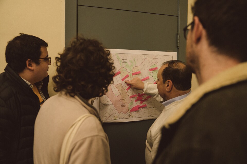 People look at a map on a wall as a man points to one part of the map.