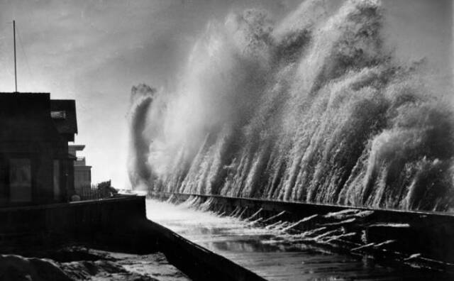 A black and white photo showing a wall of waves crashing against a sea wall in Belmont Shore, Long Beach. The waves appear to be larger than six feet tall. 
