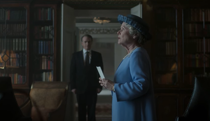 A profile of woman in a blue dress and blue hat holding a piece of paper as a man in a black suit in the distance looks at her. Book shelves line the walls.