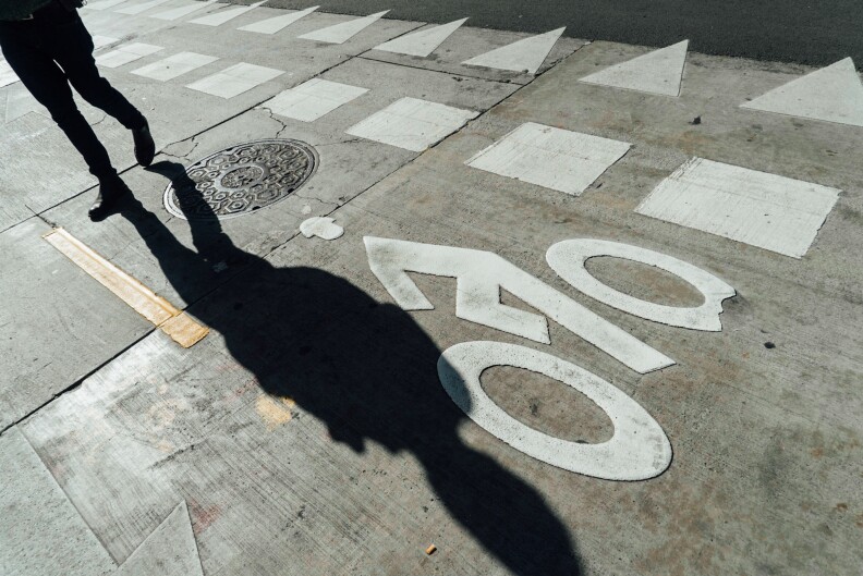 A person walks out of frame as their shadow is cast on a street, showing markings for a bike lane.