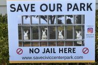 A yard sign reads 'Save Our Park, No Jail Here' with an image of rabbit statues behind bars overlaid on a park photo.