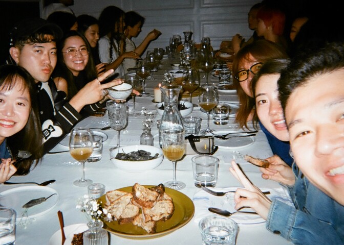 around a set table with wine glasses, dinnerware, and table bread, folks sitting around the table peer into the frame to smile
