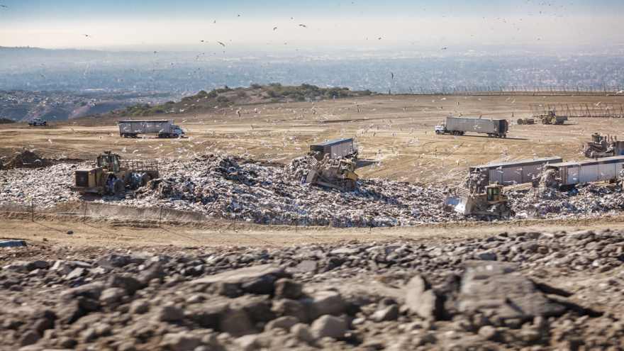 Trucks and masses of debris occupy otherwise barren, light brown land that's wide open.