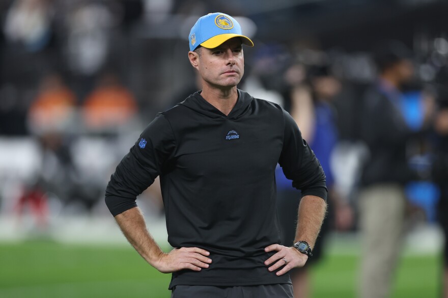 Chargers head coach Brandon Staley with his hands on his hips, wearing a black hoodie and blue and yellow Chargers hat.
