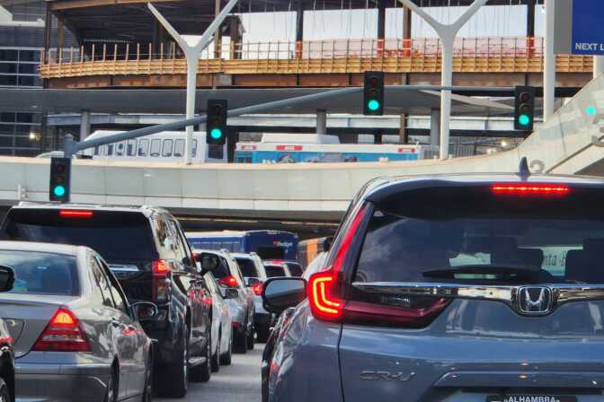 Dozens of cars in two rows fill the roads at the LAX airport. In the from of them is construction for the airport train.