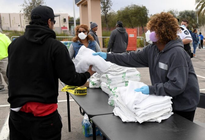 Multi-Agency Coordination Center (MACC) volunteer Bircie Wilson (R) hands out blankets as people arrive at a temporary homeless shelter set up in a parking lot at Cashman Center in Las Vegas, Nevada.