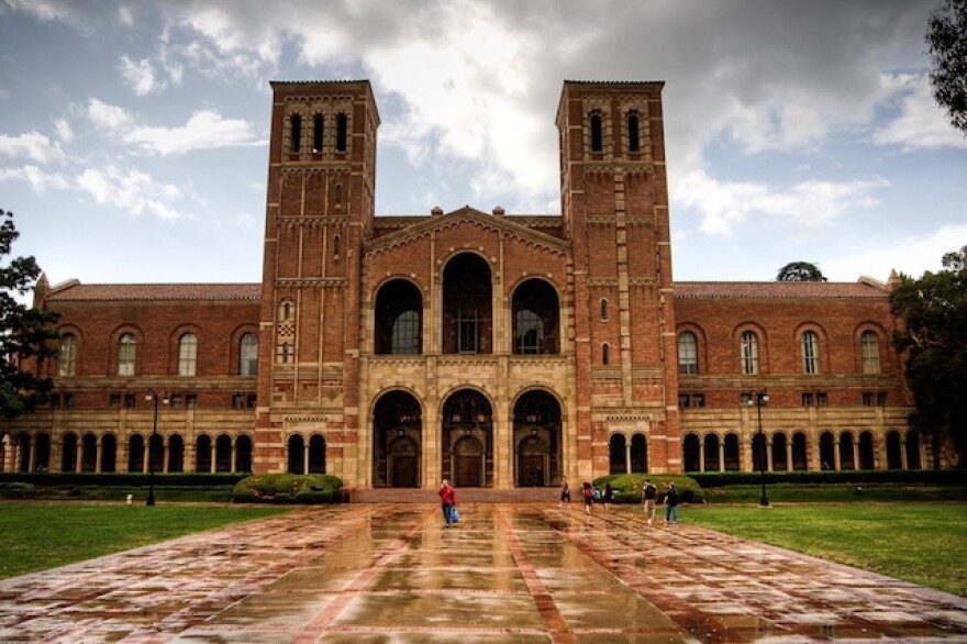 An exterior of an older brick building at UCLA. Two towers flank the entrance, which has three arched doorways.