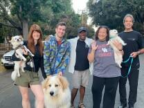 A group of five people pose with their dogs on an Altadena street. They are all smiling and one person is holding their dog. 