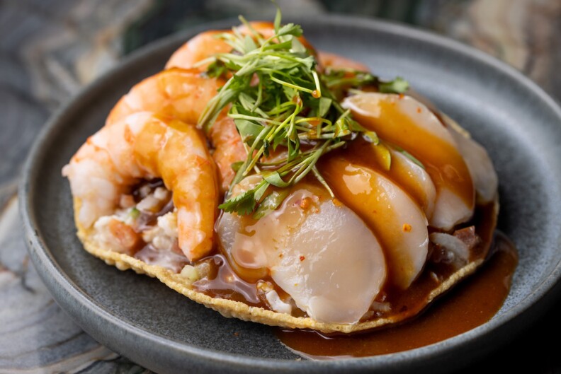 A close up shot of a tostada mixta with shrimp and fish on a gray plate.