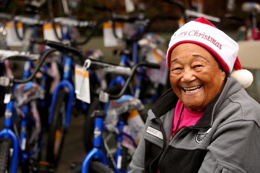 A medium dark-skinned woman is grinning at the camera while wearing a red and white Santa hat with the words "Merry Christmas" can be seen behind her, slightly out of focus.