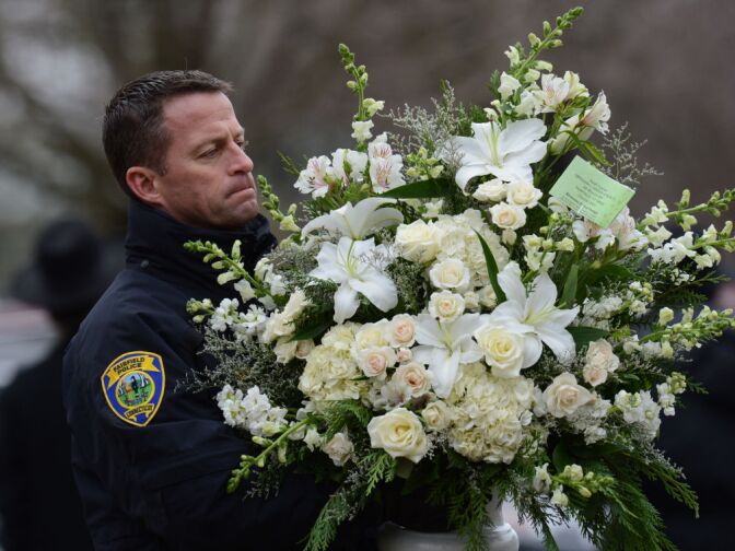 A Fairfield Police officer helps move floral arrangements following the funeral of Noah Pozner December 17, 2012 at the Abraham L. Green and Son Funeral Home in Fairfield, Connecticut. Pozner, a six year-old Jewish boy who, along with 19 other classmates and 6 teachers was murdered by a lone gunman December 14 at the Sandy Hook Elementary School in Newtown, Connecticut.