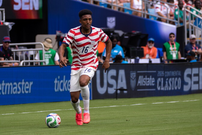 Alex Freeman kicks a soccer ball on a field in red and white horizontal stripes.