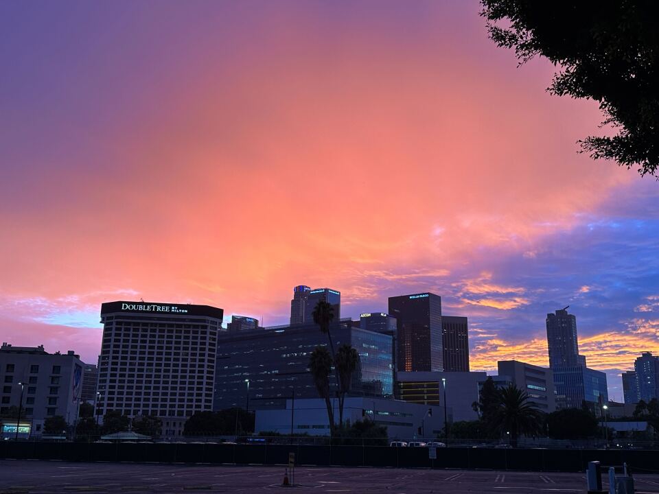 Pink and purple hued sky with buildings and a DoubleTree Hilton hotel visible in the picture. 