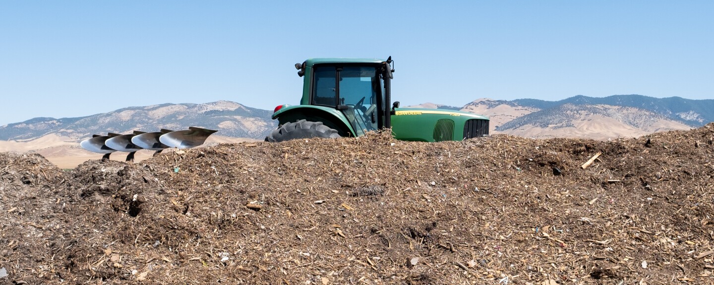 A tractor behind a pile of material with mountains in the background. 
