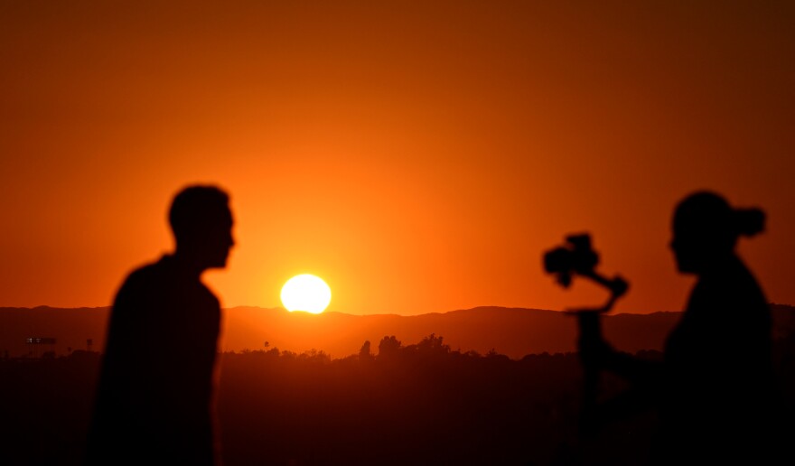 Two people are silhouetted in a red sky as the sun sets on the horizon.
