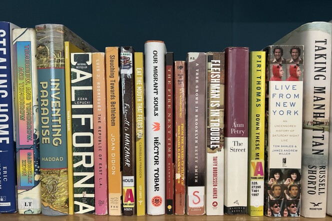 About two dozen books with titles like "Inventing Paradise," "The Republic of East L.A.," "Live from New York," and "Taking Manhattan" sit on a wooden shelf. 