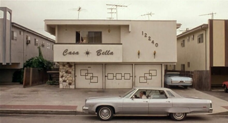 The facade of an apartment building named "Casa Bella." Vintage cars are in front and in a driveway.