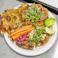 Overhead view of a white paper plate holding three tacos on crisp, griddled tortillas: one folded with melted cheese along the edges, one topped with mushrooms, refried beans, red onion, and cilantro, and one topped with grilled chicken, onion, and cilantro. Carrot sticks, pickled red onions, and lime wedges sit alongside.