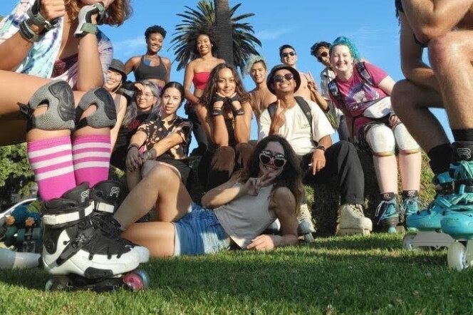 A diverse group of people in roller skates are stretched out on a lawn with palm trees behind them