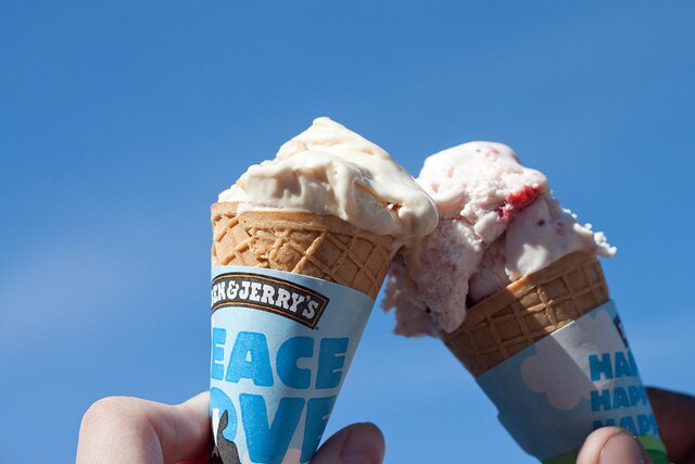 Closeup of two ice cream cones being held together. Around the sugar cones are wrappings that say "Ben and Jerry's"