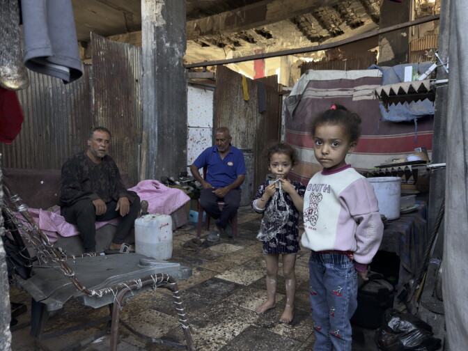 Two seated men and two young children standing, inside of a crudely constructed shelter.