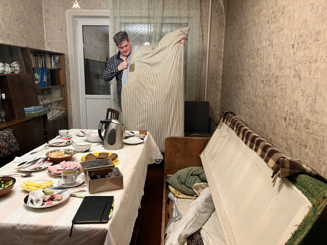 Sergey Kuznetsov holds a century-old down comforter that David Estrin made with feathers he plucked from his geese and fabric his son Jacob Estrin shipped to Ukraine from Minneapolis. Sergey's mother Lucia keeps it under the sofa in her living room in Kyiv, Ukraine.