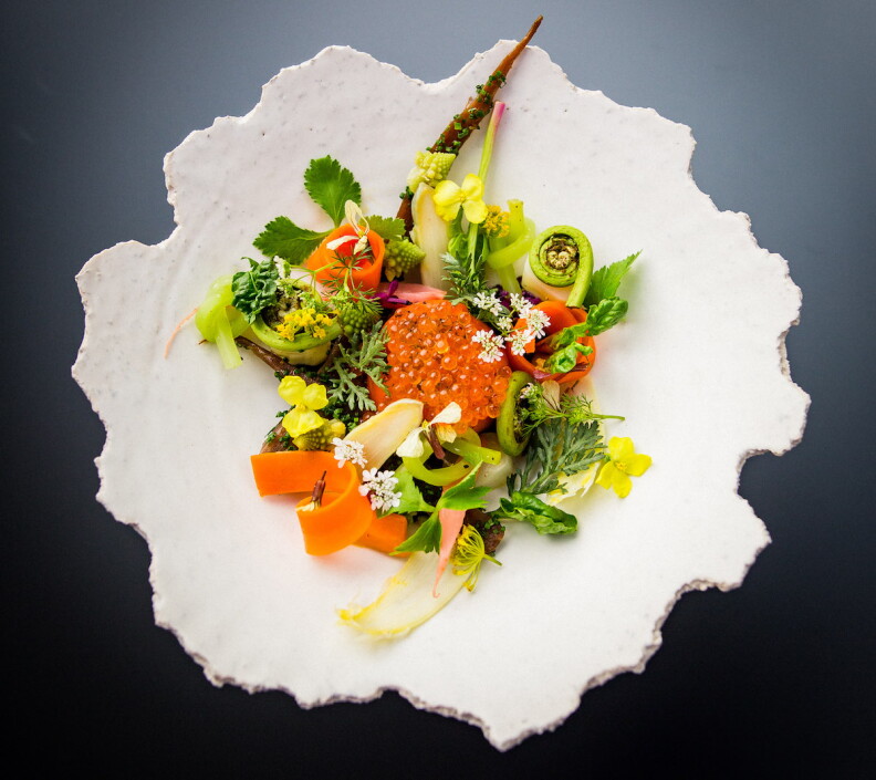A salad with greens, carrots, flowers surrounding a center of orange fish eggs.