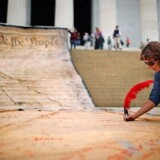 A woman signs a giant banner printed with the Preamble to the United States Constitution during a demonstration against the Supreme Court's Citizens United ruling at the Lincoln Memorial.