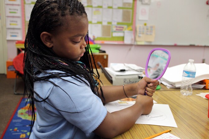 Fourth grader Samir Davis checks out her features in the mirror as she sketches. Like all the students, the nose is the hardest part.