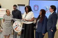 Five people stand behind a lectern with the words Inglewood Unified School District in green letters. Three women and a man have dark skin tone and one man has medium light skin tone. 