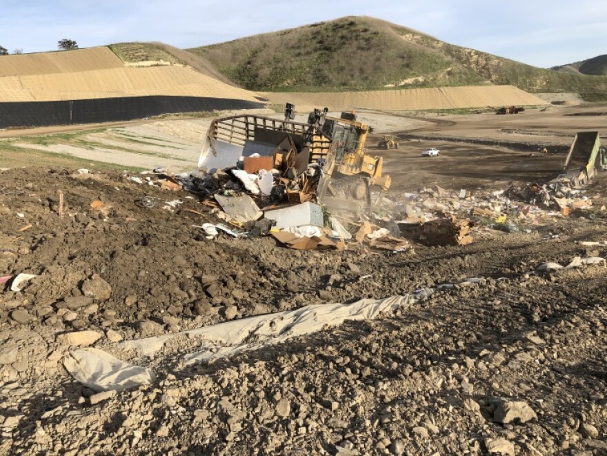 In the middle of a somewhat barren landscape, an earthmover crushes garbage.