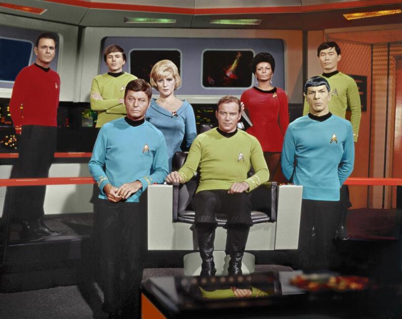 6 men and 2 women stand or sit on the bridge of a star ship. they are all wearing their star fleet uniforms