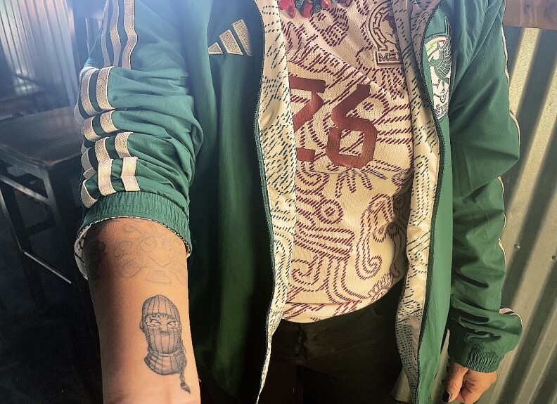A woman rolls up her sleeve to show off a tattoo of a tigress in a ski mask. 