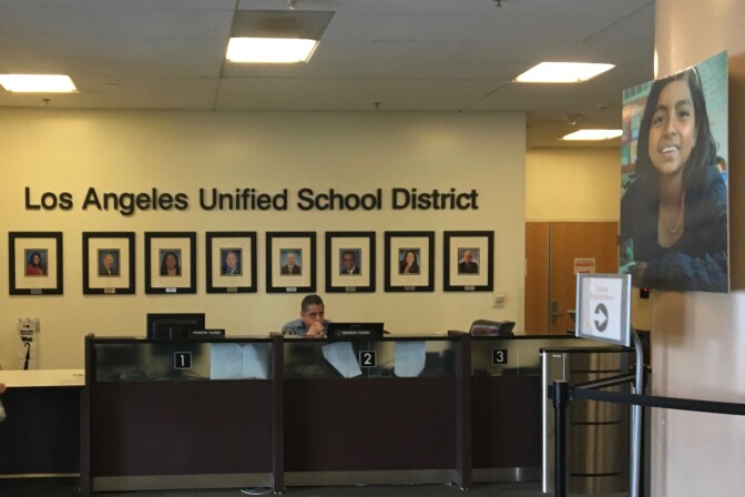 A security guard sits at a desk under a wall that says "Los Angeles Unified School District."