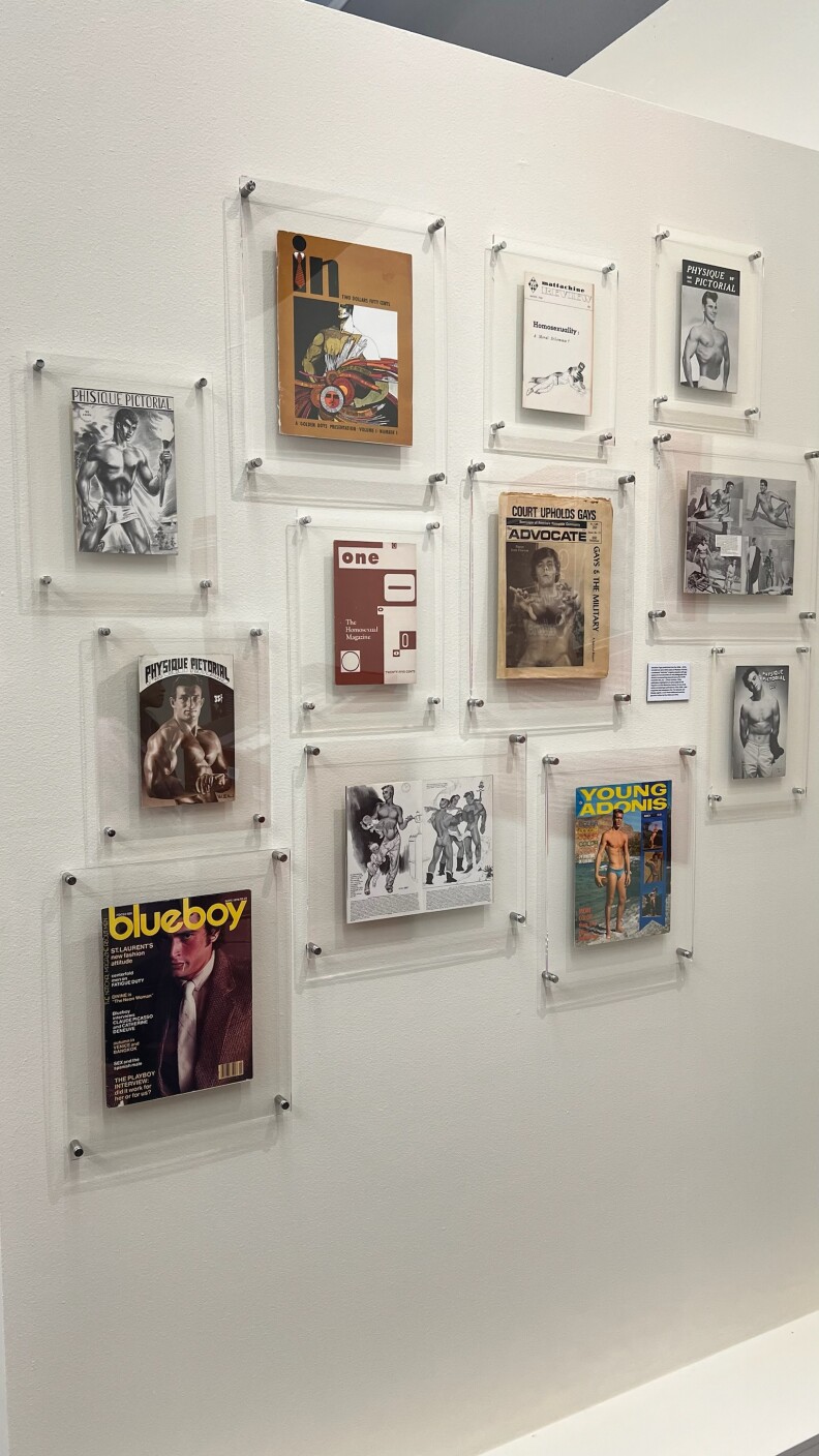 A wall with a collection of gay print material, such as magazines, newspapers, and comic books