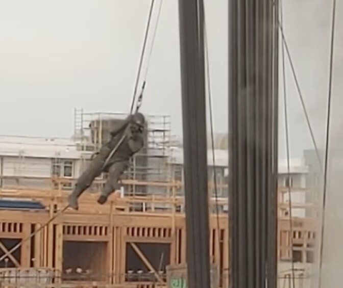 A worker uses a rope to escape an oil rig atop a blown-out oil well. The image is a screenshot from a video posted on YouTube at https://youtu.be/DW_-DTvtgy8
