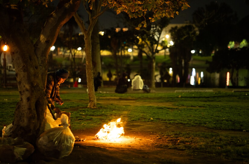 A man stands in front of a fire in a public park as other people sit on benches in the background.