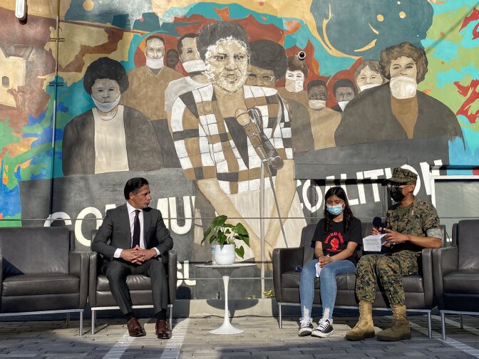 Under a mural featuring Karen Bass, the LA Unified superintendent talks with two masked students.