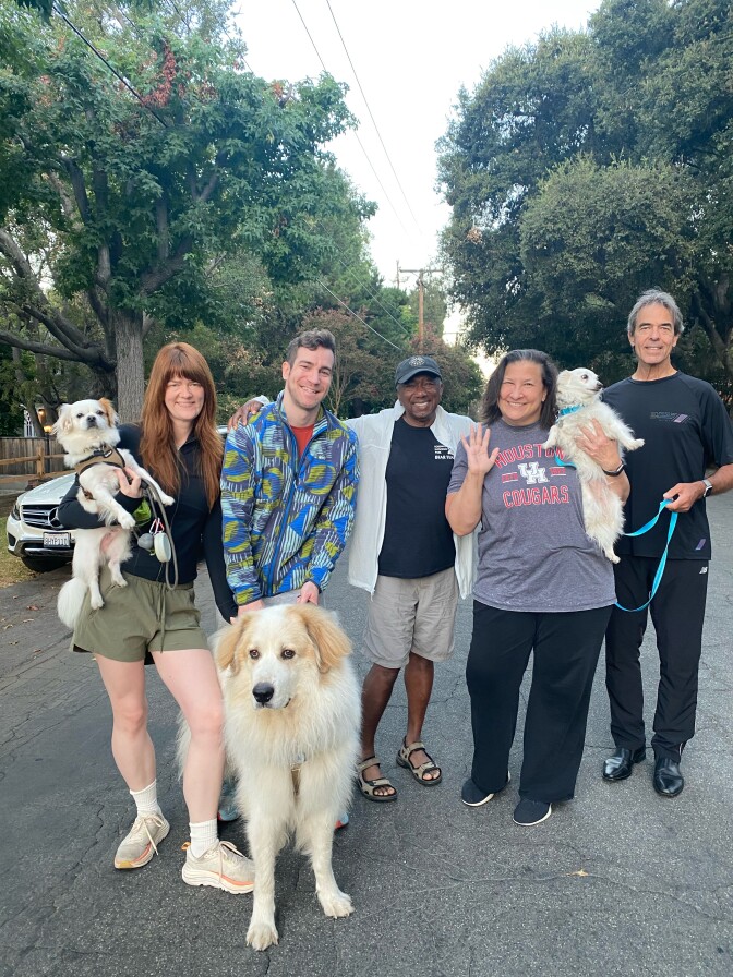 A group of five people pose with their dogs on an Altadena street. They are all smiling and one person is holding their dog. 