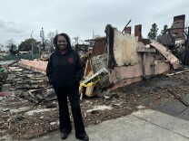  A woman stands in front of a destroyed structure in Altadena, California.
