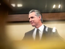 A man with salt and pepper hair, wearing a dark suit and tie, looks off to his right
