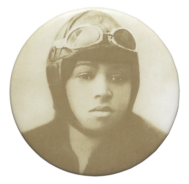 a round photo features a headshot of a Black woman wearing a leather aviator's helmet and goggles on her forehead