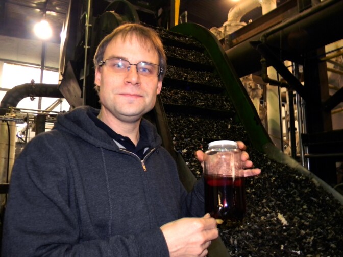 JBI CEO John Bordynuik holds a jar of No. 6 fuel oil, derived from discarded plastic like that seen on a conveyor belt at his plant.
