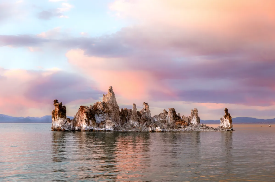A rocky outcropping juts from a lake. The sky is hazy with pink and grey clouds