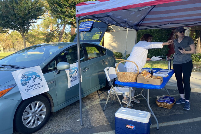 Two women stand under a pop-up shade printed with the American flag. Beside them is a car with several posters hanging from it that say "Canyon Democrats."