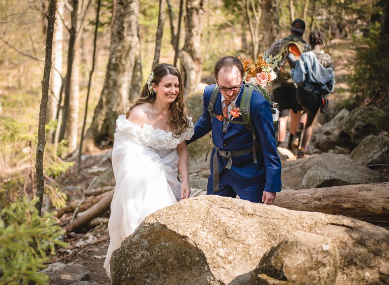 A bride and groom hike up a mountain trail in New Hampshire as part of their micro-wedding ceremony.