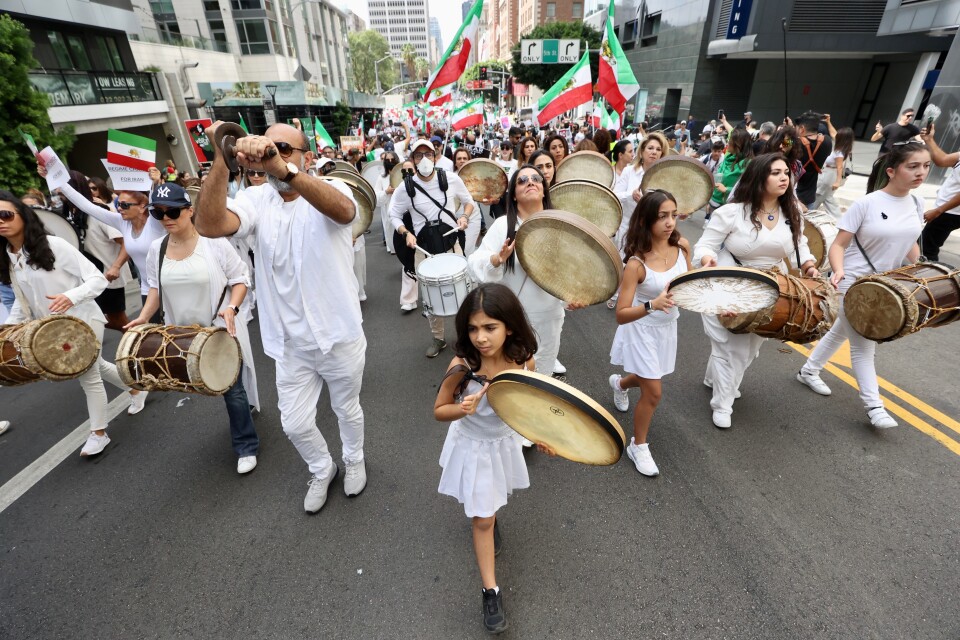 A mostly female group of drummers, women and girls, march in white on a city street.