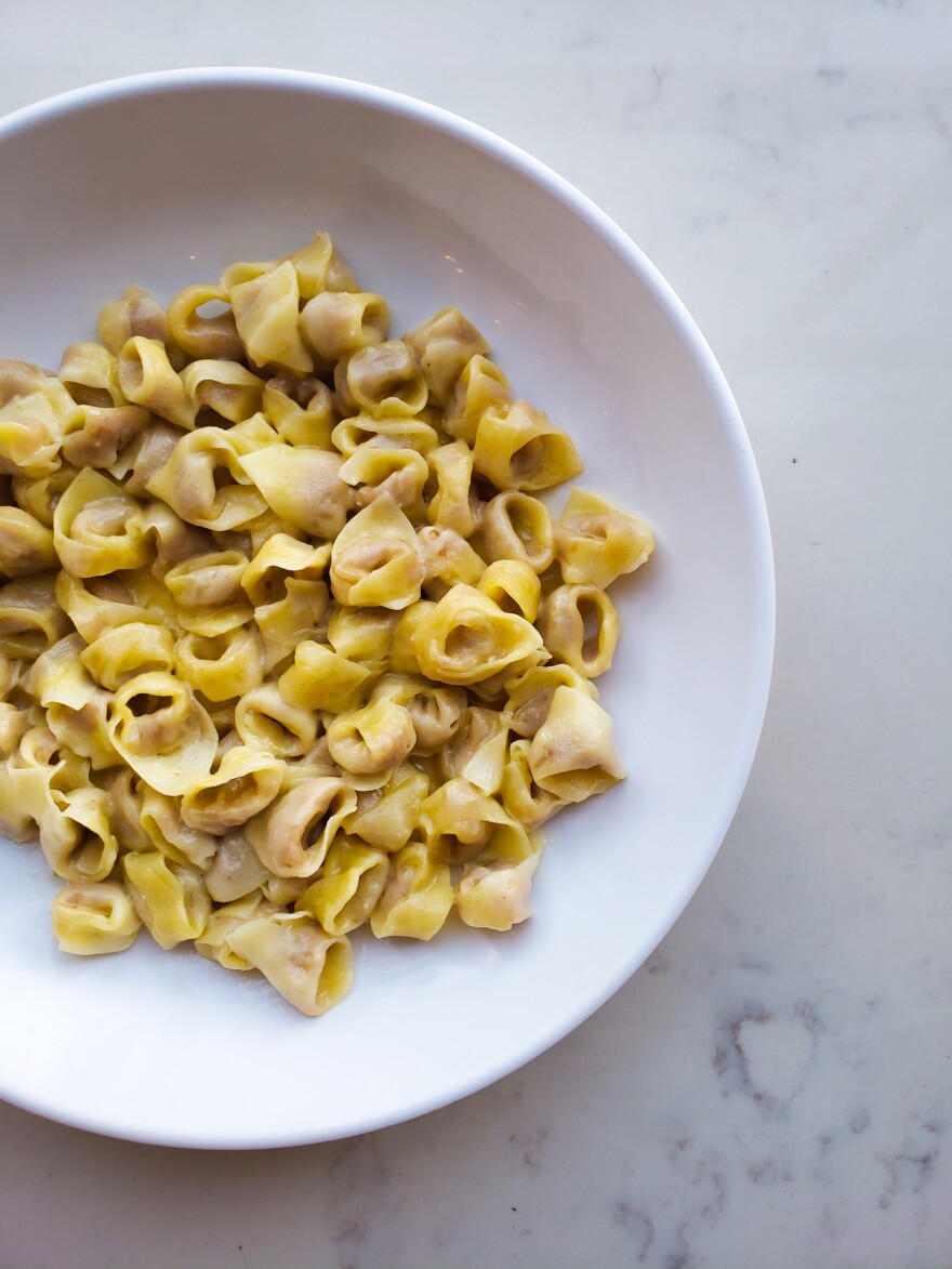 A large white bowl is filled with cooked tortellini.