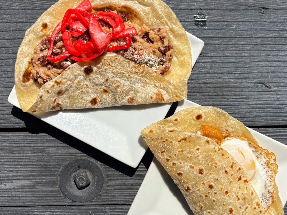 Two Honduran baleadas on white plates: one filled with beans, cheese, and topped with pickled red onions; the other with a fried egg peeking out from inside a flour tortilla.